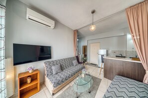 Ein modernes Wohnzimmer mit einer Couch, einem Glastisch, einem Flachbildfernseher und einer Küchenzeile mit Kühlschrank und Spüle.