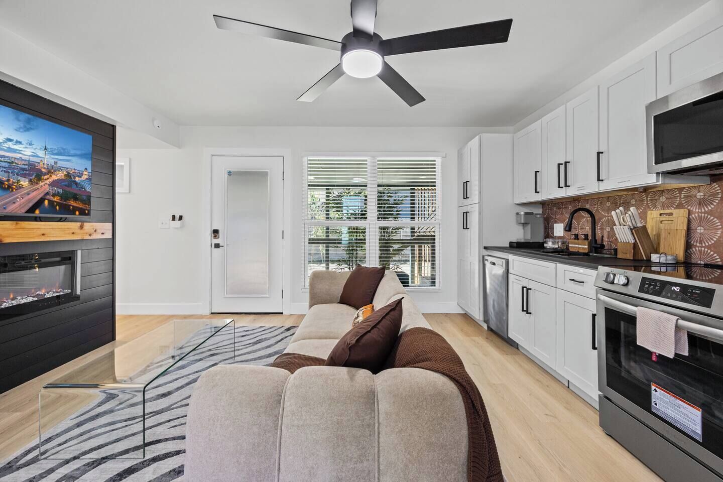 A modern living room with a sofa, a flat-screen TV, a fireplace, and a ceiling fan.