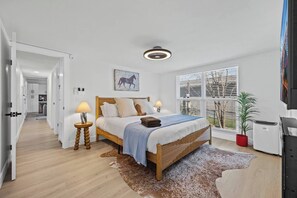 Ein Schlafzimmer mit einem Bett, Nachttischlampen, einem Teppich, einem Fenster mit Jalousien und einer Zimmerpflanze.