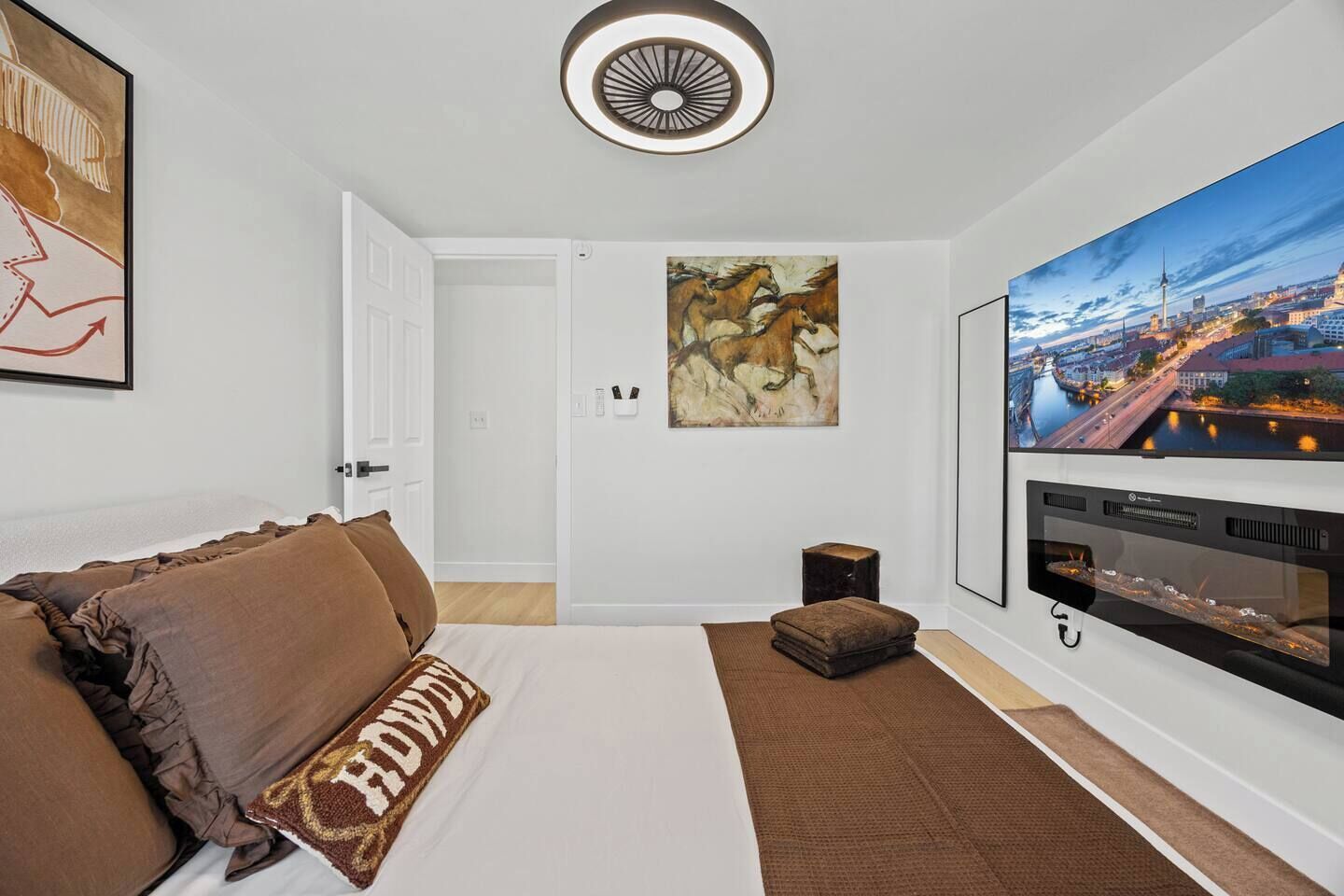 A hotel room with a bed, a TV, a painting, and a cityscape view.