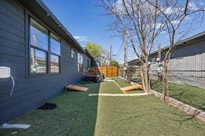Un jardin à l’arrière d’une maison d’habitation, doté d’une pelouse artificielle, d’une terrasse en bois et d’une zone délimitée par une clôture.