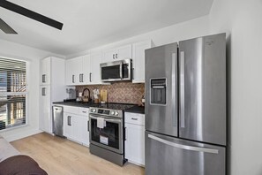 Eine moderne Küche mit weißen Schränken, Edelstahlgeräten, darunter ein Kühlschrank, eine Mikrowelle und ein Backofen, sowie einer gemusterten Spritzschutzwand.