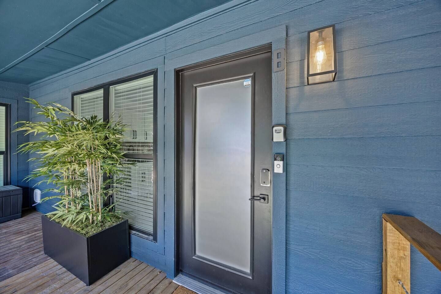 A modern exterior with a blue door, a potted plant, and a wooden deck.