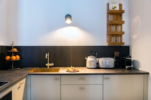 Une cuisine moderne équipée d’un évier encastré, d’une bouilloire, d’un grille-pain et d’une étagère où sont rangés des verres.