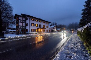 Un edificio de dos pisos con el suelo cubierto de nieve, una calle pavimentada al frente y un cielo despejado.