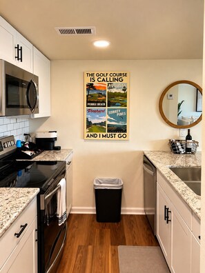 A kitchen with white cabinets, a black microwave, a stainless steel stove, a trash bin, and a wall-mounted poster advertising golf courses.