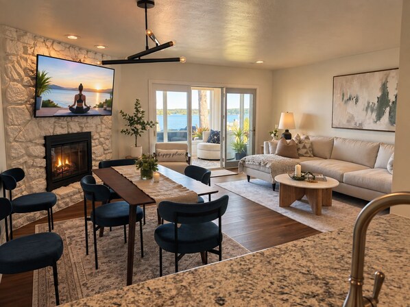 A living room with a stone wall, a fireplace, a TV, a sofa, a coffee table, and a dining area with chairs.
