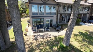 A two-story house with a patio area featuring outdoor furniture and a large sliding glass door. - Updated Large Lakefront Townhouse with Bald Eagle Views overlooking Grand Lake. (Afton)