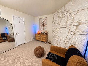 A modern living room with a stone wall, a wooden dresser, a mirror, and a sofa with a decorative pillow.