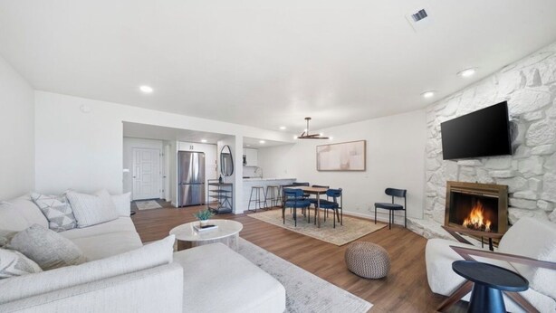 A modern living room with a fireplace, a dining area, and a kitchen in the background. - Updated Large Lakefront Townhouse with Bald Eagle Views overlooking Grand Lake. (Afton)