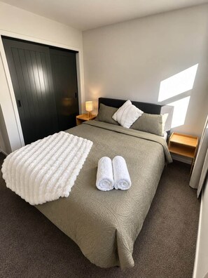 Ein Hotelzimmer mit Bett, Nachttisch, Lampe, Fenster mit Tageslicht und Tür.