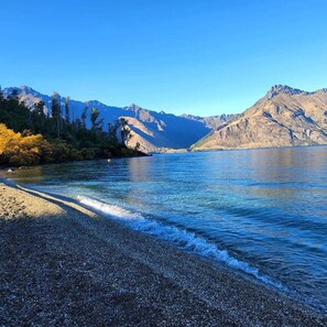 Ein See mit kiesigem Ufer und Bergen im Hintergrund.