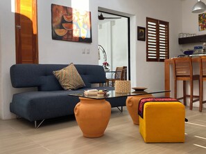 Ein modernes Wohnzimmer mit einem blauen Sofa, einem orangefarbenen Hocker und einem Glastisch.
