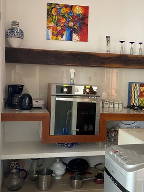 Eine Küche mit Kaffeemaschine, Herd und Mikrowelle. Zudem Regale mit Dekoration und ein Bild an der Wand.