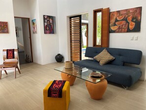 Ein modernes Wohnzimmer mit einer Couch, einem Glastisch, einem Holzstuhl und einem gelben Hocker.