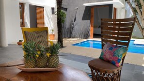 Ein Poolbereich mit Holzstuhl, Tisch und einer Ananas als Dekoration, mit Blick auf ein Schwimmbecken.