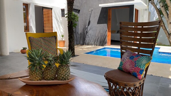 Ein Poolbereich mit Holzstuhl, Tisch und einer Ananas als Dekoration, mit Blick auf ein Schwimmbecken.