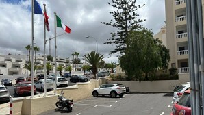A parking lot with multiple cars and a motorcycle, surrounded by buildings and palm trees. - Castle Comfort (Los Cristianos)