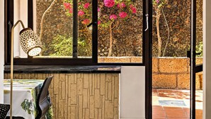 A room with a view of pink flowers through a window, a wall with a textured pattern, and a table with a tablecloth. - Castle Comfort (Los Cristianos)