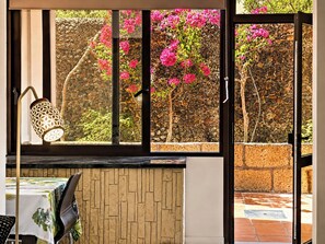 Ein Zimmer mit Blick auf rosa Blüten durch ein Fenster, eine Wand mit einer strukturierten Oberfläche und ein Tisch mit Tischdecke.