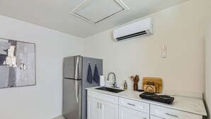 Eine moderne Küche mit einem Edelstahl-Kühlschrank, weißen Schränken, einer integrierten Spüle und einer Wand-Klimaanlage.