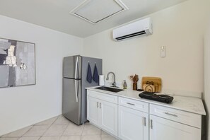 Eine moderne Küche mit einem Edelstahl-Kühlschrank, weißen Schränken, einer integrierten Spüle und einer Wand-Klimaanlage.