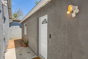 Ein Wohnhausfassade mit einer weißen Tür, einer Betonwand, einem Blumentopf und einer Wandleuchte.