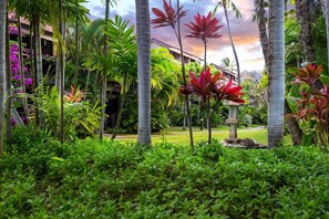 A lush garden with palm trees, a stone lantern, and a building with a red roof. - Tropical Garden Vibes Maui (Kihei)