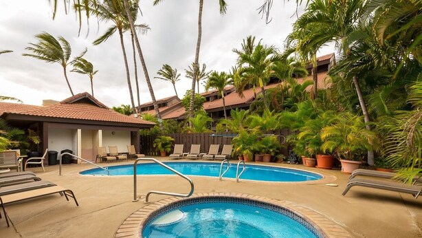 A swimming pool area with lounge chairs and a hot tub, surrounded by palm trees and a building with a tiled roof. - Tropical Garden Vibes Maui (Kihei)