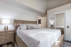 A bedroom with a bed, a nightstand, a lamp, a wardrobe, and a mirror. - Tropical Garden Vibes Maui (Kihei)