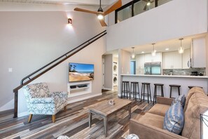 En moderne stue med sofa, sofabord, fjernsyn og trappe.