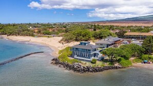 A coastal property with a beach, a large house with a balcony, and a rocky shoreline. - Tropical Garden Vibes Maui (Kihei)
