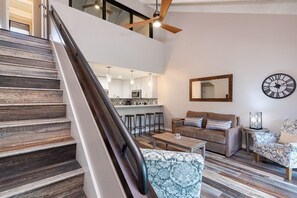 Een modern interieur met een trap, een keuken, een zithoek met een bank en een gestreept fauteuil, en een wandklok.