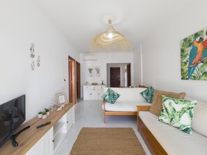 A modern bedroom with a bed, a TV, and a dining area in the background. - Casa das Conchas T2 by YHA (Conceiçao de tavira)