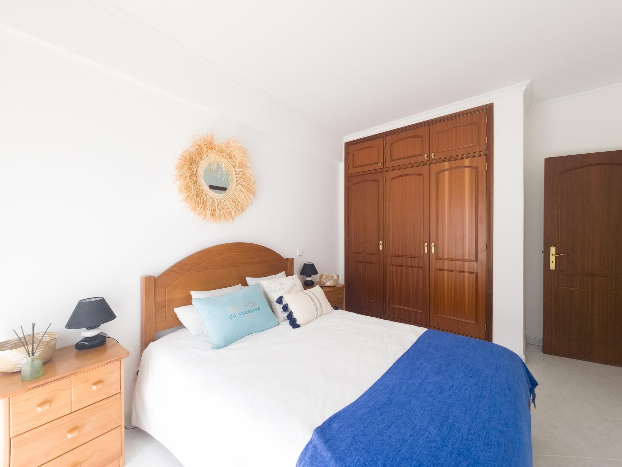 Une chambre à coucher avec un lit en bois, une table de chevet avec une lampe, un miroir fixé au mur et une armoire.