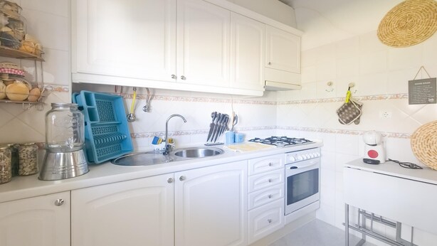 A kitchen with white cabinets, a sink, a stove, and various kitchen utensils. - Casa das Conchas T2 by YHA (Conceiçao de tavira)