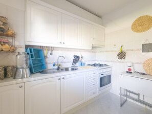 A kitchen with white cabinets, a sink, a stove, and various kitchen utensils. - Casa das Conchas T2 by YHA (Conceiçao de tavira)
