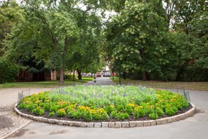 Ein kreisrunder Blumenbeet mit verschiedenen Blumen und einem gepflasterten Weg zu einem Gebäude.