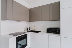 Eine moderne Küche mit weißen Schränken, einer schwarzen Kochfeld, einem eingebauten Backofen, einer schwarzen Mikrowelle und einem goldenen Wasserhahn.
