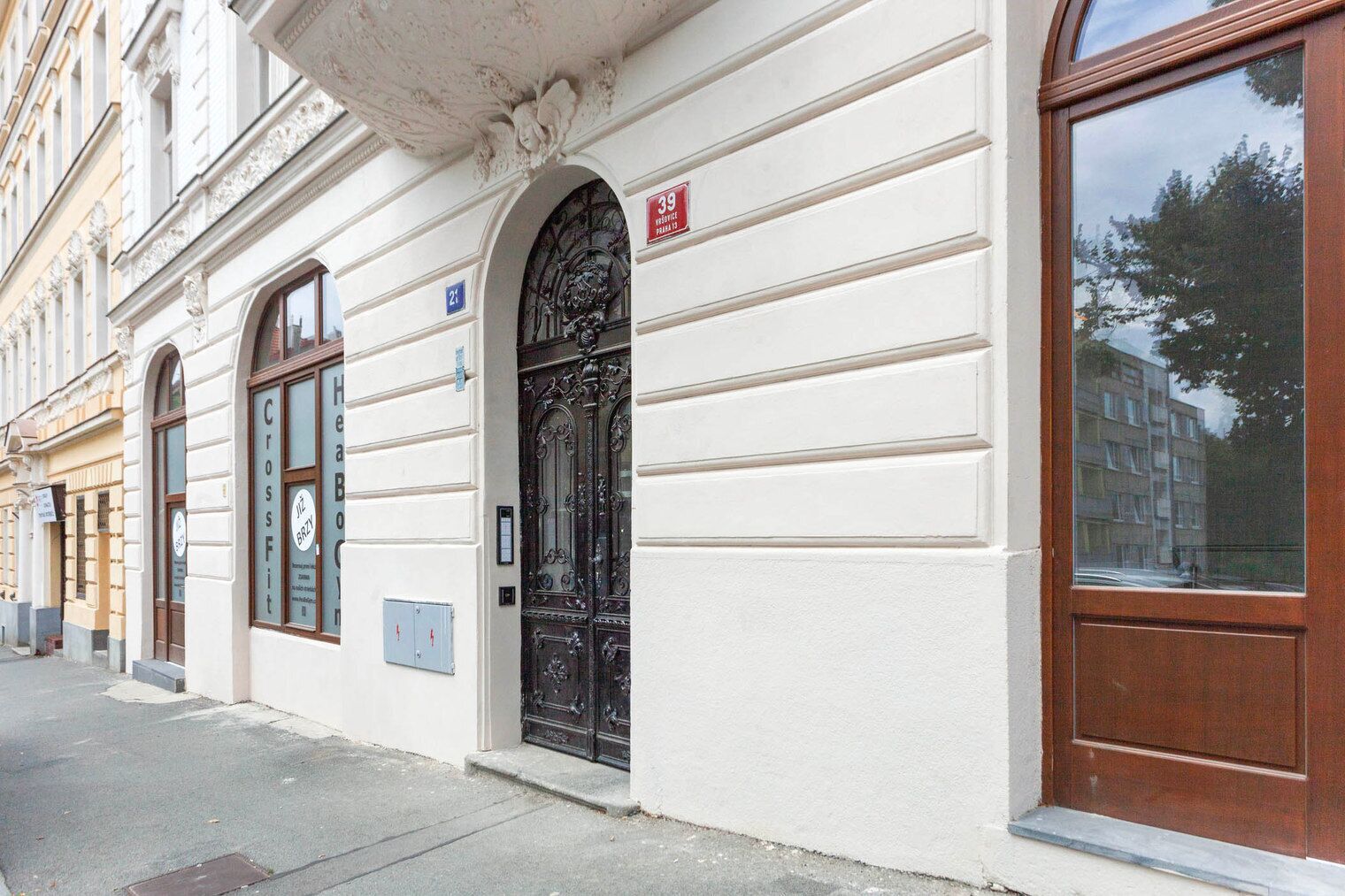 A building facade with a large arched window, a door with a metal gate, and a sign indicating the address.