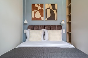 A bed with a brown headboard, white bedding, and a gray quilt. There are two wall-mounted light fixtures and abstract art above the bed. - Blueground | Nusle, view, furnished nr Vysehrad (PRG-70) (Prague)