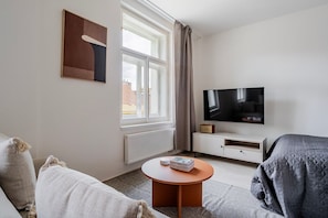 A hotel room with a bed, a TV, a small table with books, a window with curtains, and a radiator. - Blueground | Nusle, view, furnished nr Vysehrad (PRG-70) (Prague)
