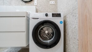 A front-loading washing machine in a modern kitchen with a granite countertop and a white cabinet. - Blueground | Nusle, view, furnished nr Vysehrad (PRG-70) (Prague)