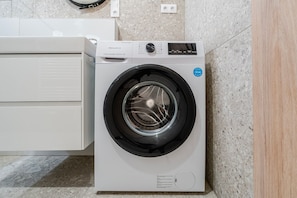A front-loading washing machine in a modern kitchen with a granite countertop and a white cabinet. - Blueground | Nusle, view, furnished nr Vysehrad (PRG-70) (Prague)