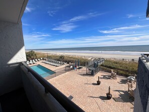 Uma área de piscina com espreguiçadeiras e vista para a praia.