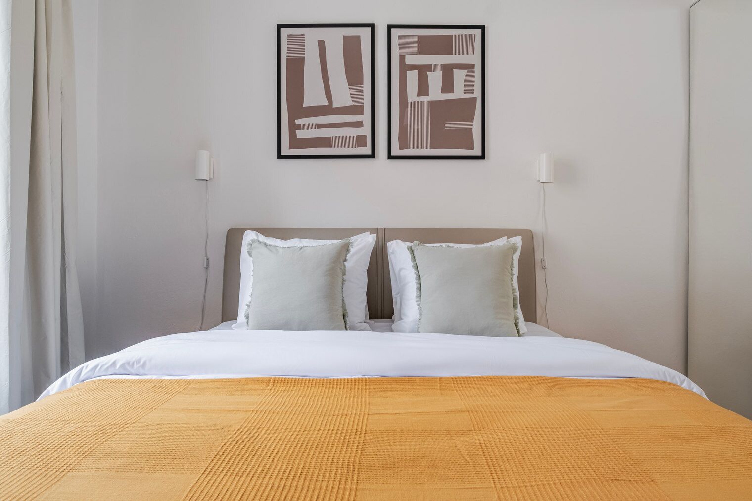 Une chambre d’hôtel avec un lit, deux oreillers, une tête de lit et deux tableaux abstraits accrochés au mur.