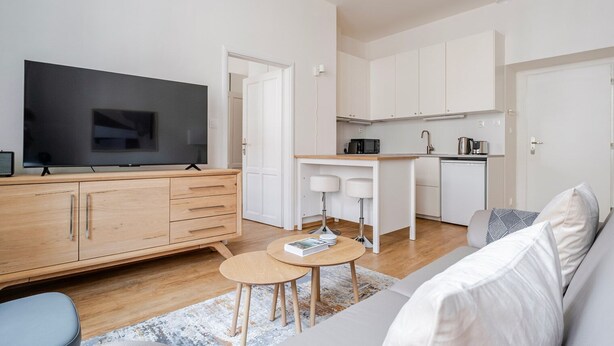 Ett modernt vardagsrum med en platt-TV, ett träskåp, ett litet runt bord och en soffa.