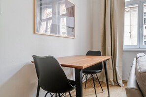 Ein Essbereich mit einem Holztisch und zwei schwarzen Stühlen, einem gerahmten Bild an der Wand und einem Fenster mit Vorhängen.
