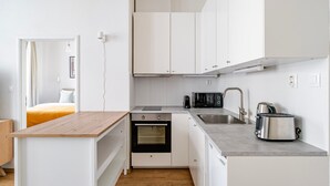 Ett kompakt kök med vita skåp, en inbyggd ugn, en mikrovågsugn, en vattenkokare och en brödrost.
