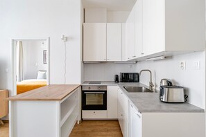 Eine kleine Küche mit weißen Schränken, einem Einbauofen, einer Mikrowelle, einem Wasserkocher und einem Toaster.
